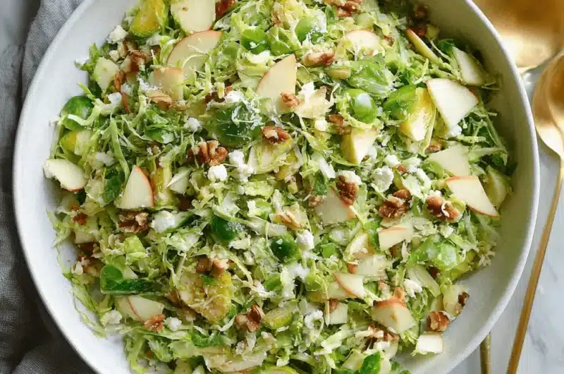 Overhead photograph of a hearty shaved brussels sprouts salad with apple slices, pecans, and feta cheese.