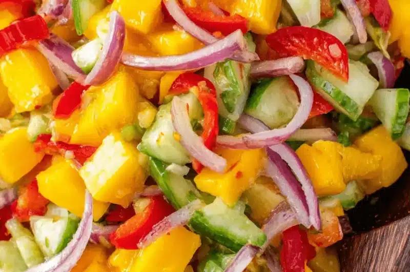 Close-up of a vibrant, chunky tropical mango salad with cucumber, red onion, and chili served in a rustic stoneware bowl.