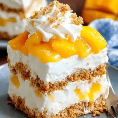 Close-up of a layered square slice of creamy, chilled no-bake mango float dessert with graham cracker layers, fresh mango chunks, and a whipped cream topping.