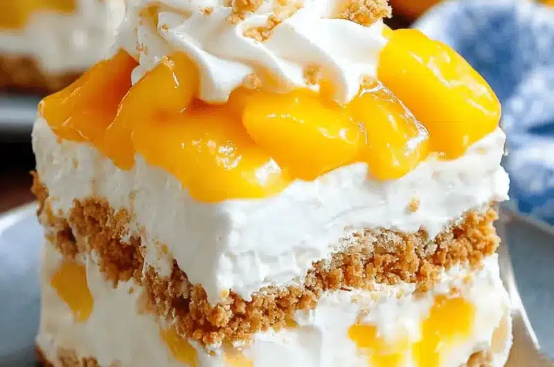 Close-up of a layered square slice of creamy, chilled no-bake mango float dessert with graham cracker layers, fresh mango chunks, and a whipped cream topping.