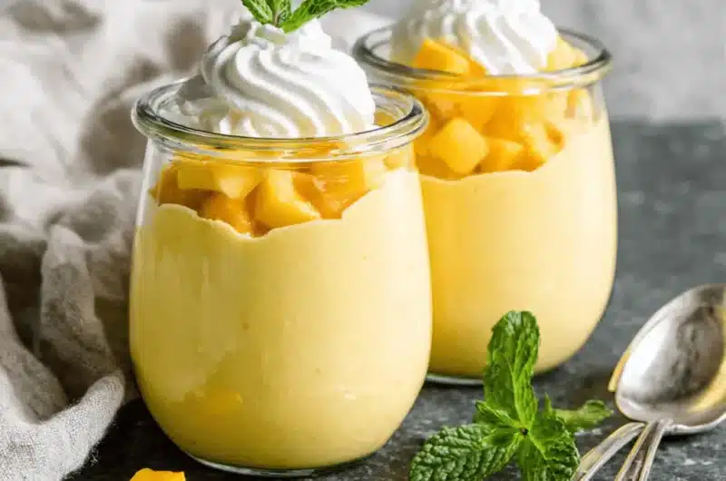 Detailed photograph of two layered glass jars holding a luxurious creamy mango dessert, garnished with fresh mint.