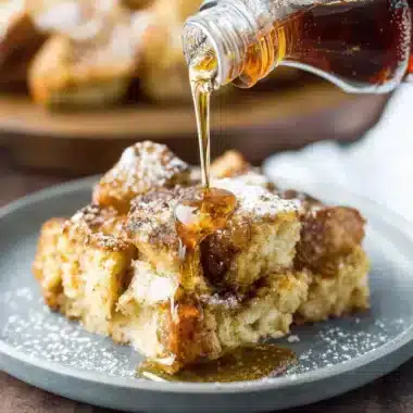 Amazing Foolproof French Toast Casserole 4 Close-up of golden French Toast Casserole drizzled with glistening maple syrup on a rustic plate.