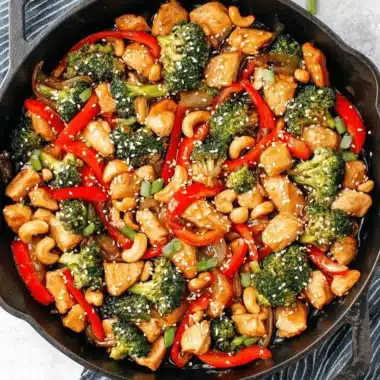 Overhead shot of a glossy Cashew chicken stir fry with vibrant red peppers and broccoli served in a cast-iron skillet.