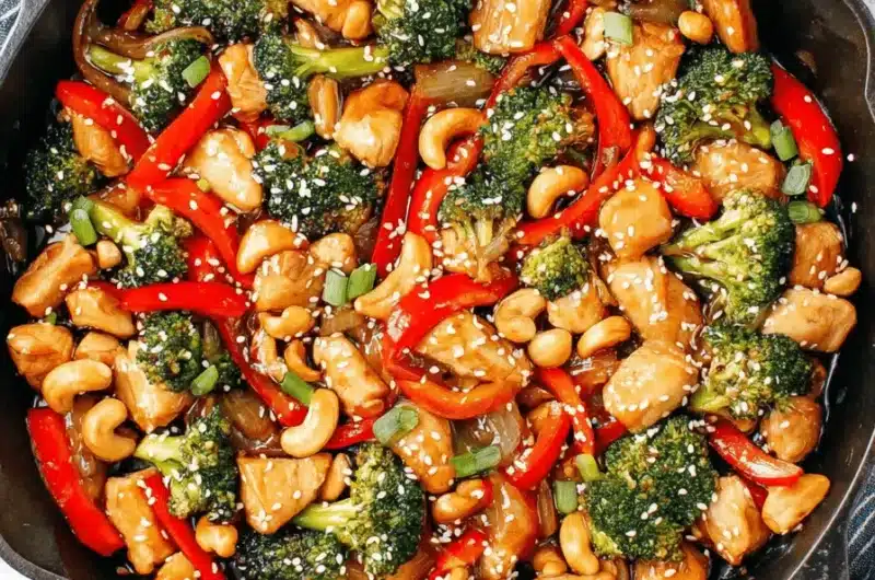 Overhead shot of a glossy Cashew chicken stir fry with vibrant red peppers and broccoli served in a cast-iron skillet.
