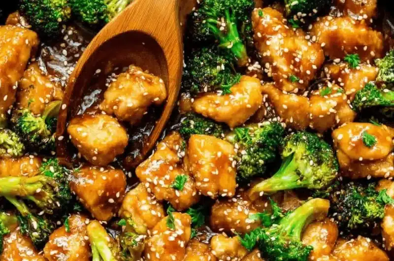 Appetizing close-up of glossy, sesame-covered chicken and broccoli stir fry served hot in a black cast-iron skillet.