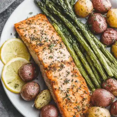 Herb-crusted roasted salmon fillet served with vibrant green asparagus spears and seasoned new potatoes, highlighting a healthy, plated meal of salmon and asparagus.