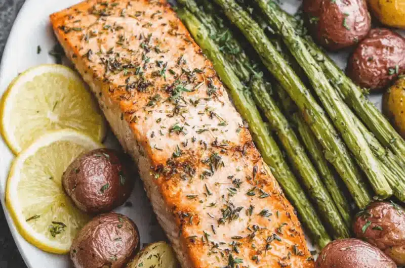 Herb-crusted roasted salmon fillet served with vibrant green asparagus spears and seasoned new potatoes, highlighting a healthy, plated meal of salmon and asparagus.