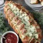 Appetizing close-up of cheesy, pull-apart christmas tree bread served on a slate platter with a side of marinara dipping sauce.