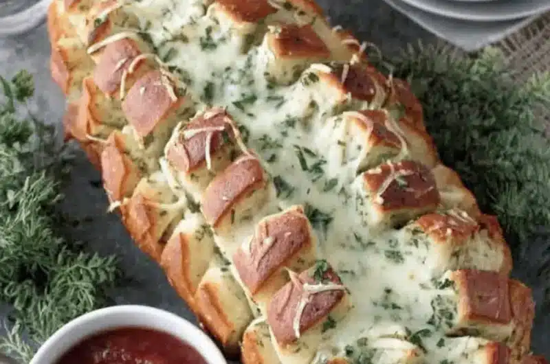 Appetizing close-up of cheesy, pull-apart christmas tree bread served on a slate platter with a side of marinara dipping sauce.