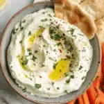 Rustic bowl of creamy, freshly made whipped feta dip garnished with olive oil, served alongside pita bread and fresh vegetable crudités.