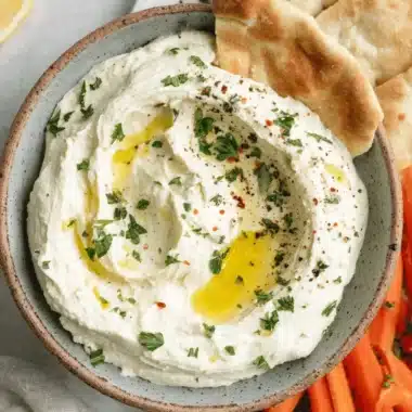 The Ultimate Whipped Feta Dip: Simple & Creamy 4 Rustic bowl of creamy, freshly made whipped feta dip garnished with olive oil, served alongside pita bread and fresh vegetable crudités.