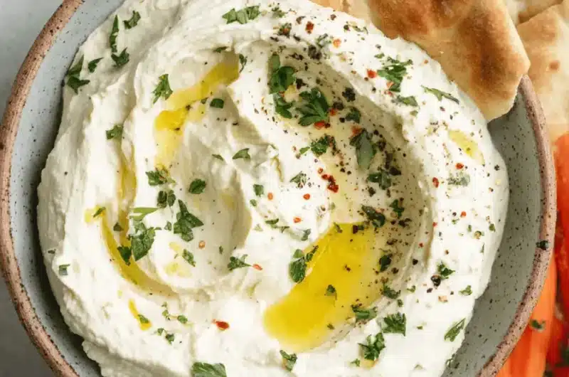 Rustic bowl of creamy, freshly made whipped feta dip garnished with olive oil, served alongside pita bread and fresh vegetable crudités.
