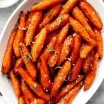 Vibrant close-up of perfectly roasted honey glazed carrots with sea salt and fresh herbs in a white dish.