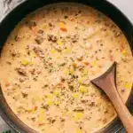 Overhead photo of hearty, creamy shepherds pie soup filled with ground beef, potatoes, corn, and peas in a dark Dutch oven.