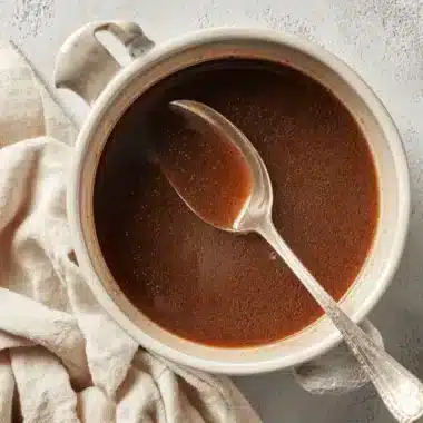 Overhead view of a rustic pot filled with rich, dark Beef au Jus and an antique silver spoon.