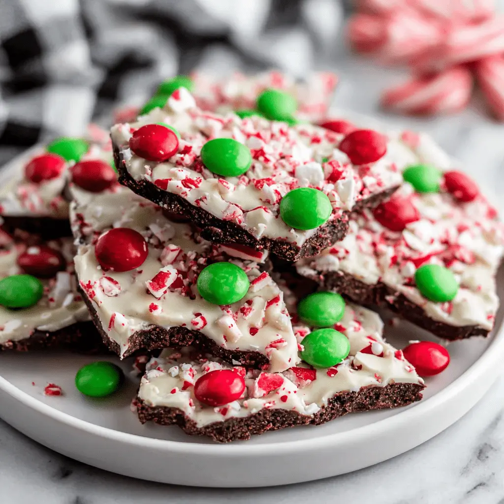 The Ultimate Peppermint Bark Recipe 2 Appetizing close-up of festive Peppermint Bark pieces with dark chocolate, white chocolate, crushed candy canes, and colorful red and green candies on a white plate.