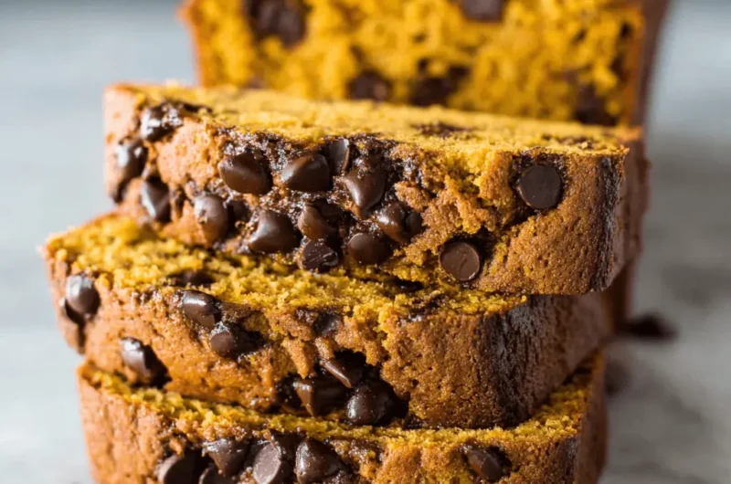 Stack of three moist slices of homemade pumpkin chocolate chip bread on a light surface, with the loaf in the background.