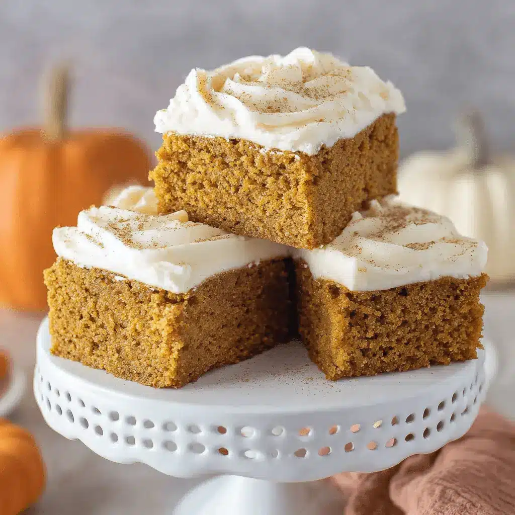 Three frosted pumpkin bars dusted with spice on a decorative white cake stand, surrounded by autumn pumpkins.