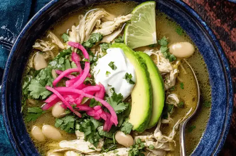 Hearty bowl of green chili chicken soup garnished with avocado, pickled onions, and fresh cilantro on a dark background.