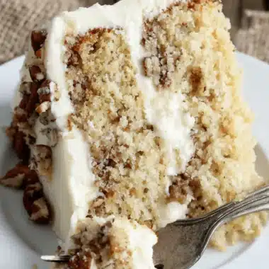 Ultimate Hummingbird Cake: Easy Southern Dessert 4 Close-up of a slice of classic layered hummingbird cake with cream cheese frosting and chopped pecans on a white plate.