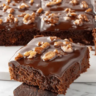 Easy & Foolproof Texas Sheet Cake Recipe 4 Decadent slice of Texas Sheet Cake with chocolate glaze and chopped walnuts on a silver dessert server.