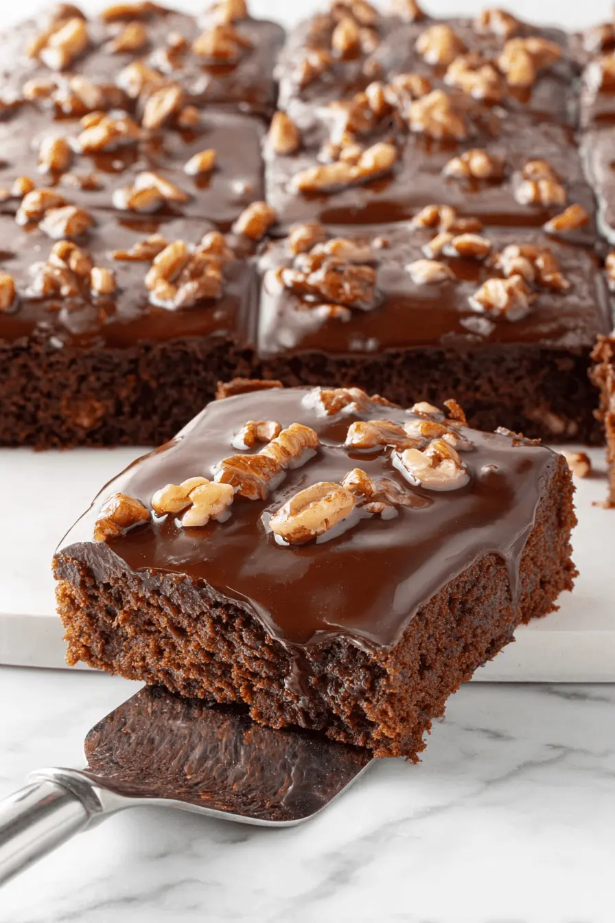 Easy & Foolproof Texas Sheet Cake Recipe 2 Decadent slice of Texas Sheet Cake with chocolate glaze and chopped walnuts on a silver dessert server.