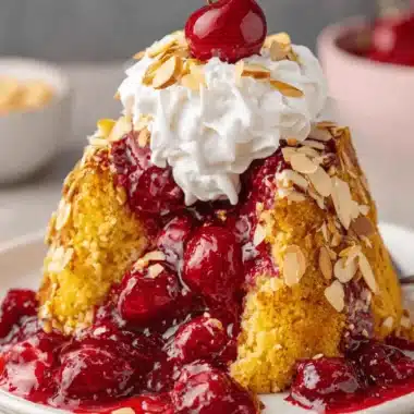 Ultimate Easy Cherry Dump Cake Recipe 3 Close-up of a golden brown, crumbly cherry dump cake topped with whipped cream and fresh cherries.