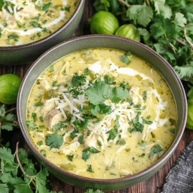Close-up photo of creamy green enchilada chicken soup in rustic bowls, topped with shredded cheese and fresh cilantro.