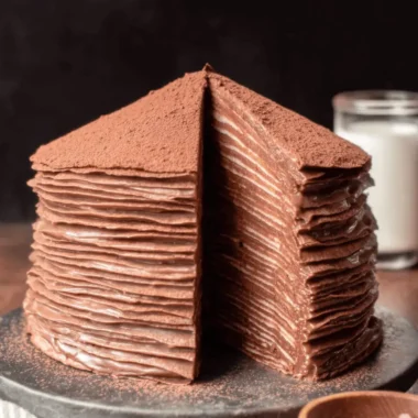The Ultimate Easy Mille Crepe Cake Recipe 3 A multi-layered chocolate mille crepe cake dusted with cocoa powder, revealing its intricate structure of crepes and cream.
