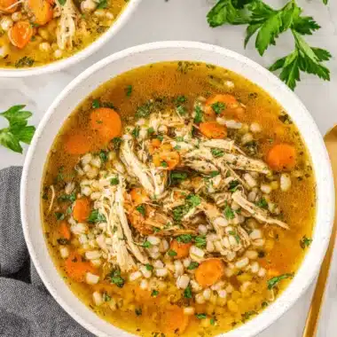 The Ultimate Chicken Barley Soup Recipe 3 Hearty homemade Chicken Barley Soup with shredded chicken, carrots, and fresh parsley in a white ceramic bowl on a marble background.