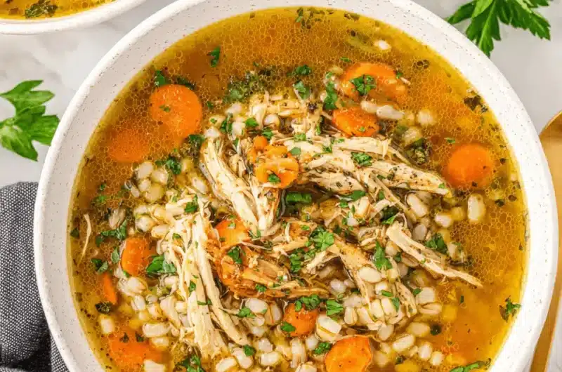 Hearty homemade Chicken Barley Soup with shredded chicken, carrots, and fresh parsley in a white ceramic bowl on a marble background.