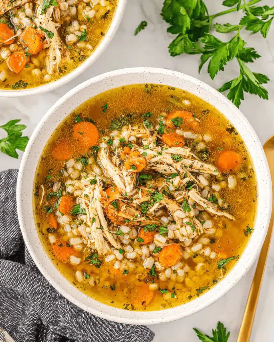 Hearty homemade Chicken Barley Soup with shredded chicken, carrots, and fresh parsley in a white ceramic bowl on a marble background.