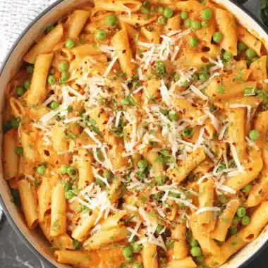 The Ultimate Spicy Rigatoni Pasta Recipe 4 Close-up of creamy, spicy rigatoni pasta in a black pot, topped with grated Parmesan, fresh herbs, and red pepper flakes.