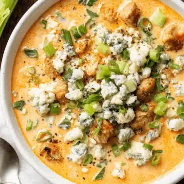 The Ultimate Foolproof Buffalo Chicken Soup 4 Overhead view of a creamy, richly garnished bowl of homemade Buffalo Chicken Soup topped with large crumbles of blue cheese and fresh green scallions.