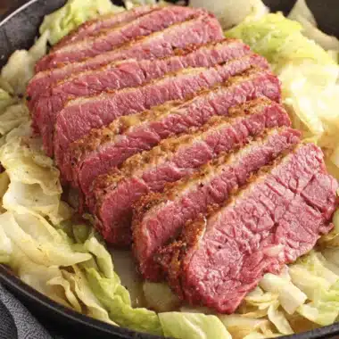 Amazing Slow Cooker Corned Beef and Cabbage 4 Hearty, thinly sliced corned beef and cabbage meal served in a rustic black cast-iron skillet on a wooden surface.
