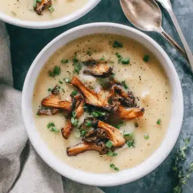 The Ultimate Dairy Free Potato Soup Recipe 4 Overhead view of a creamy, gourmet bowl of dairy free potato soup garnished with crispy wild mushrooms and fresh chives.