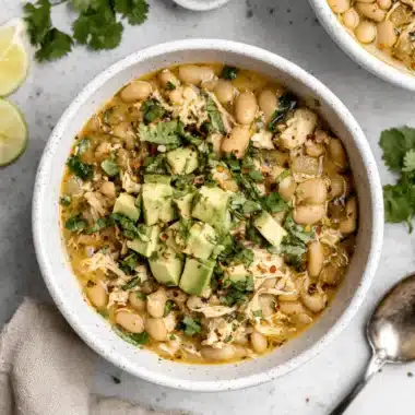 The Ultimate Creamy White Bean Chicken Chili Recipe 3 Hearty bowl of White Bean Chicken Chili, garnished with fresh avocado and cilantro on a light stone surface.
