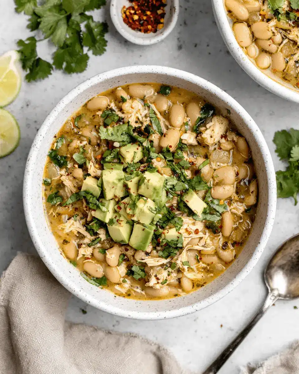 The Ultimate Creamy White Bean Chicken Chili Recipe 2 Hearty bowl of White Bean Chicken Chili, garnished with fresh avocado and cilantro on a light stone surface.