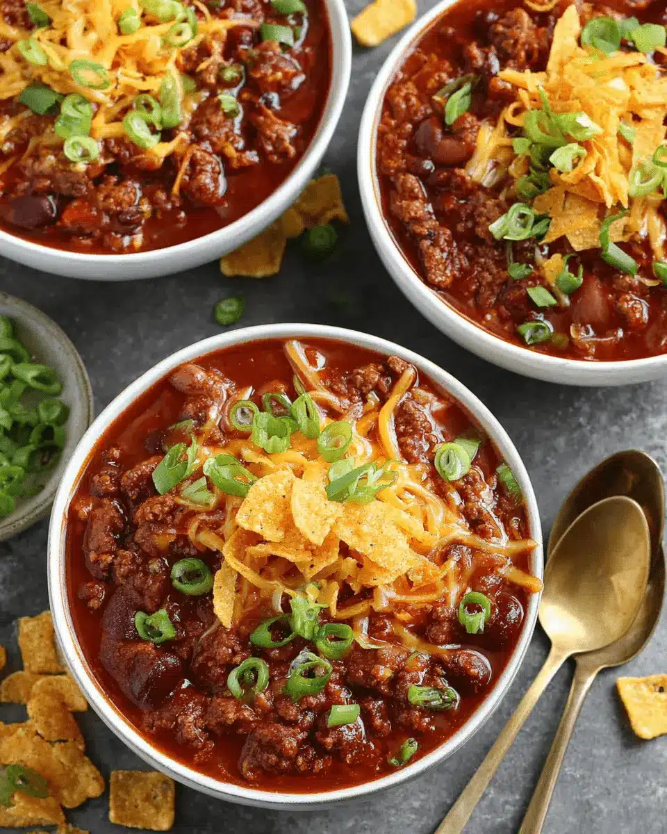The Ultimate Foolproof Beef Chili Recipe 2 Hearty bowl of beef chili recipe topped with melted cheese, tortilla chips, and green onions on a dark background.