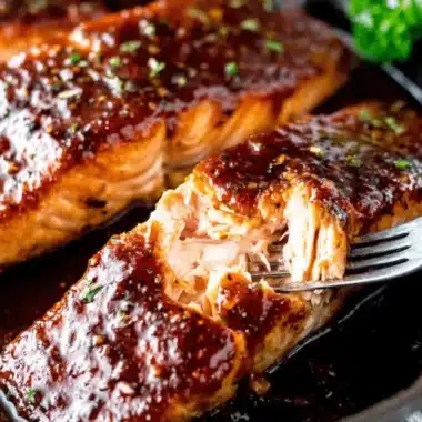 Close-up of perfectly cooked, moist Honey Glazed Salmon fillets flaking under a fork, garnished with fresh herbs.