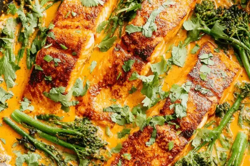 Pan-seared salmon curry served directly in a black skillet, featuring thick salmon fillets, broccolini, and fresh cilantro garnish.