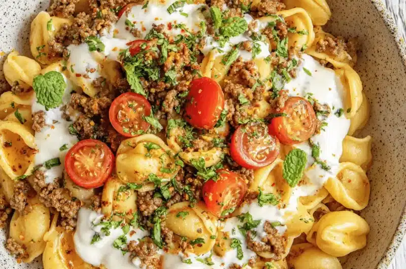 Detailed overhead view of a rustic bowl containing savory Turkish Pasta (Orecchiette) topped with ground meat, creamy yogurt, fresh parsley, and mint.