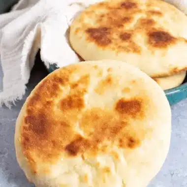 Foolproof Sourdough Pita Bread: Perfect Puff! 3 Freshly baked Sourdough Pita Bread with visible golden char marks, resting next to a stack in a vibrant teal ceramic bowl.