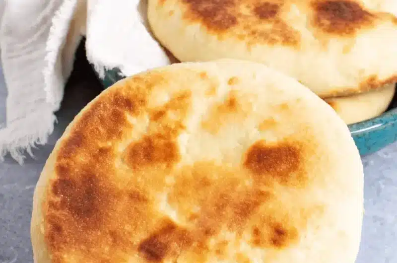 Freshly baked Sourdough Pita Bread with visible golden char marks, resting next to a stack in a vibrant teal ceramic bowl.