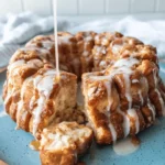 Golden-brown Sourdough Monkey Bread being glazed with white icing and warm caramel sauce on a rustic blue plate.
