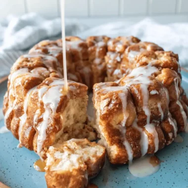 The Ultimate Foolproof Sourdough Monkey Bread 4 Golden-brown Sourdough Monkey Bread being glazed with white icing and warm caramel sauce on a rustic blue plate.