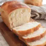Freshly baked, golden-crusted Sourdough Potato Bread sliced on a dark wooden cutting board.