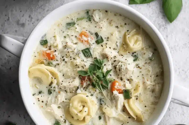 Overhead flat lay photo of a creamy bowl of hearty Chicken Tortellini Soup garnished with fresh thyme and cracked pepper.