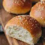 Ultimate Sourdough Hamburger Buns: Easy Recipe 5 Freshly baked Sourdough Hamburger Buns topped with sesame seeds displayed on a rustic wooden board, showing the soft, airy crumb structure.