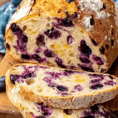 Vibrant Lemon Blueberry Sourdough Bread 4 Slices of freshly baked lemon blueberry sourdough bread on a rustic wooden board, showing the airy crumb and deep purple blueberries.
